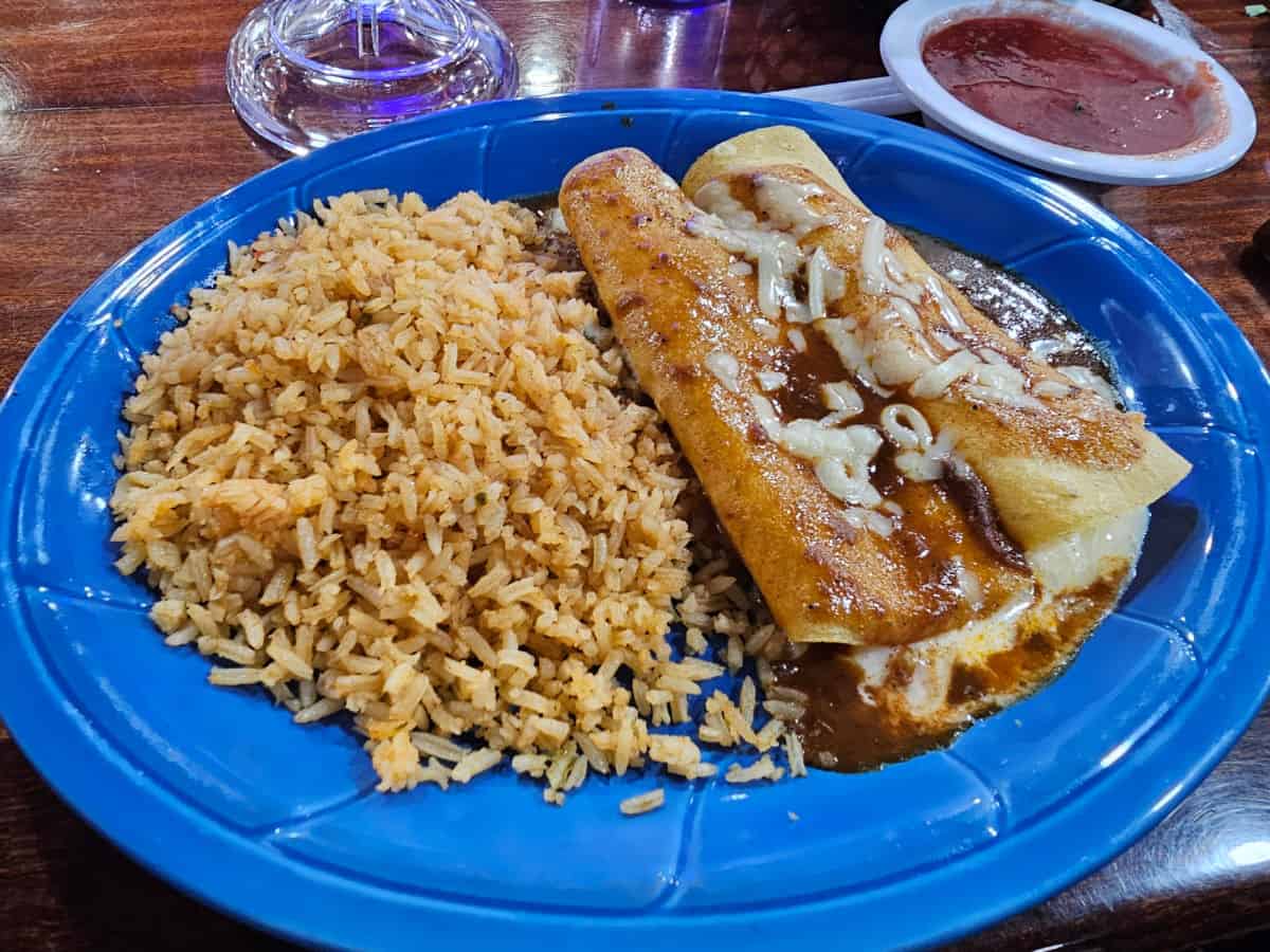 cheese enchiladas and rice on a blue plate next to a bowl of salsa