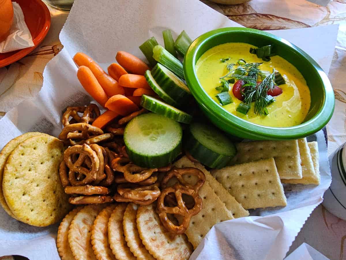 dill dip in a green bowl with cucumbers, carrots, crackers, and pretzels