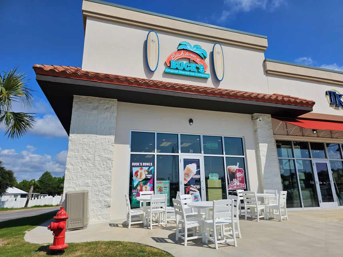 Bahama Buck's Sign with surfboards over the restaurant entrance with white tables and chairs outside