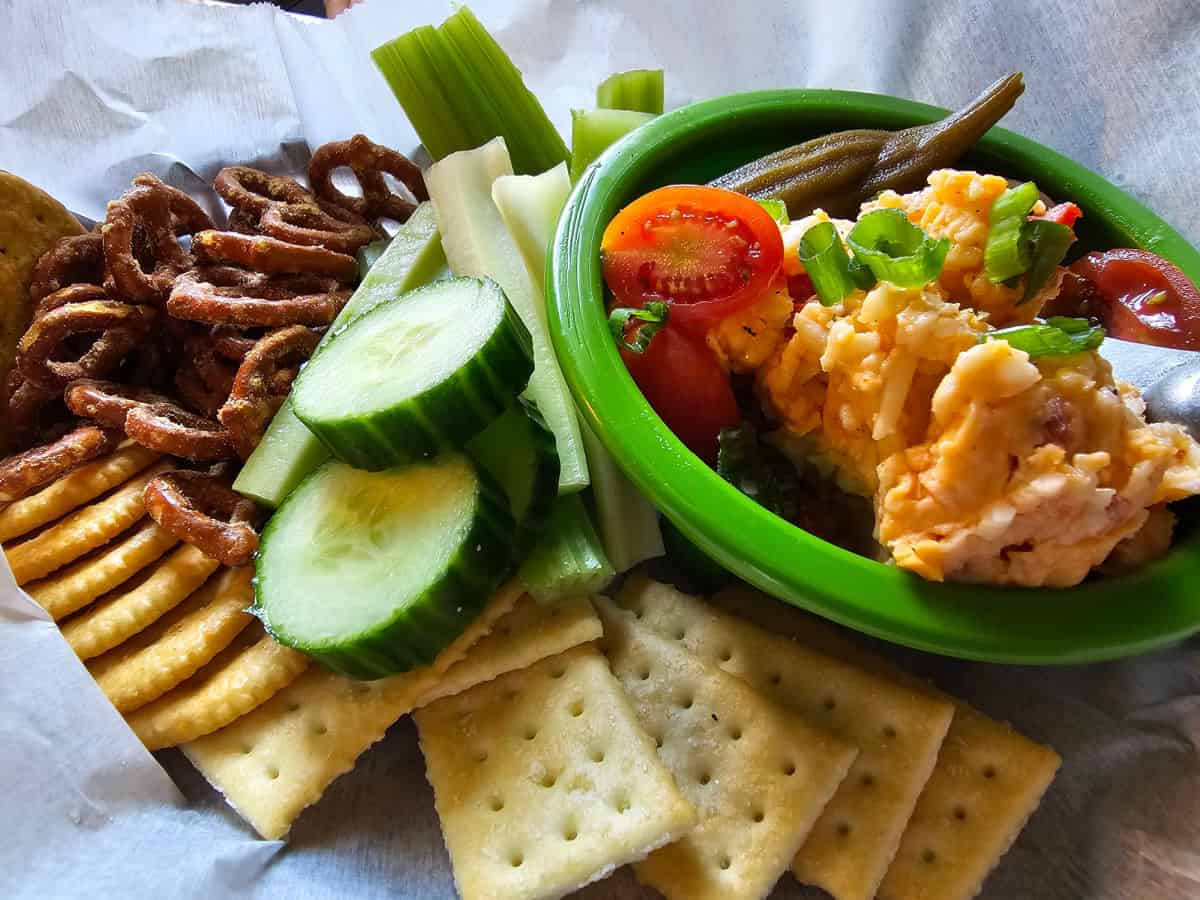 Pimento cheese dip in a green bowl, next to cucumbers, crackesr, and pretzels