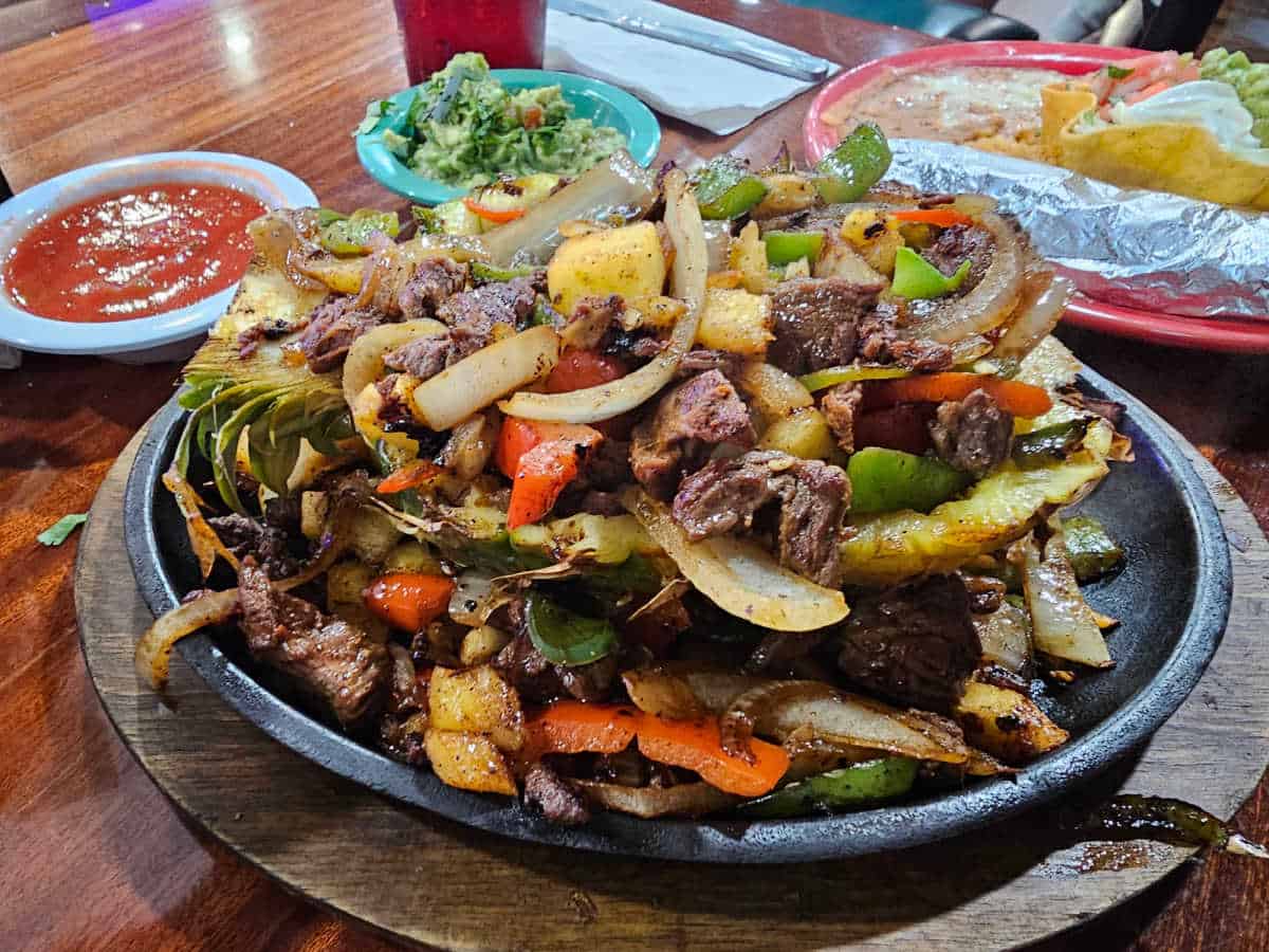fajitas in a pineapple on a skillet on the table next to chips and salsa