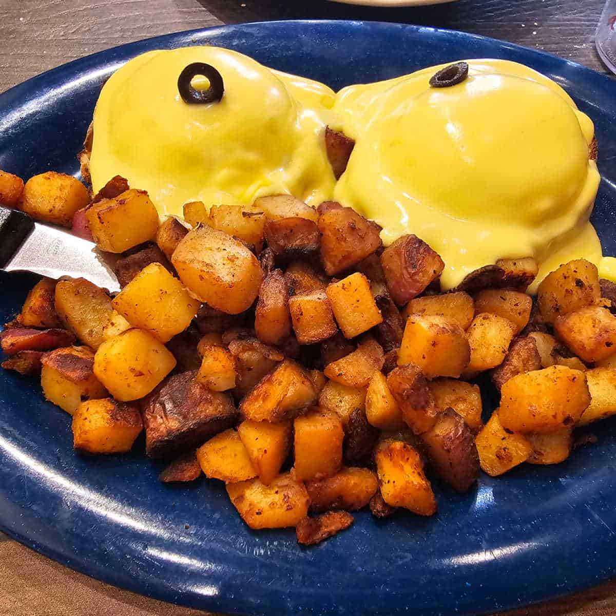 eggs benedict with home fries on a blue plate