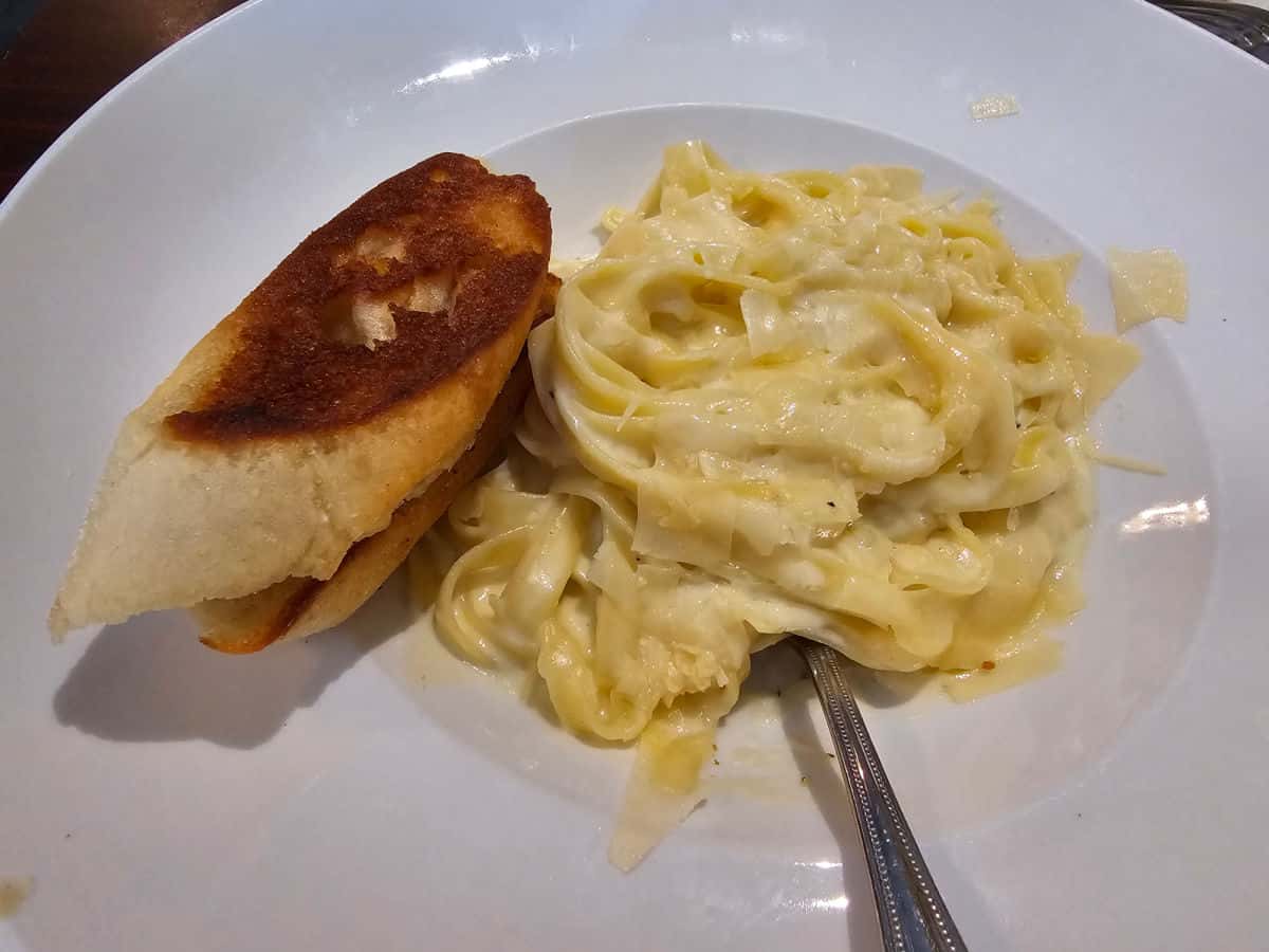Fettuccine alfredo on a white plate wtih garlic bread