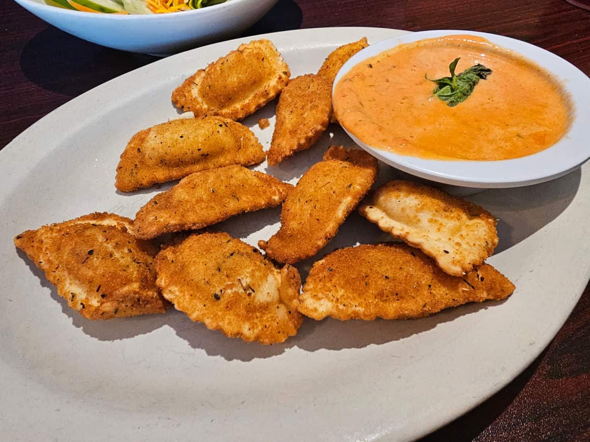 fried ravioli on a white plate with a bowl of sauce