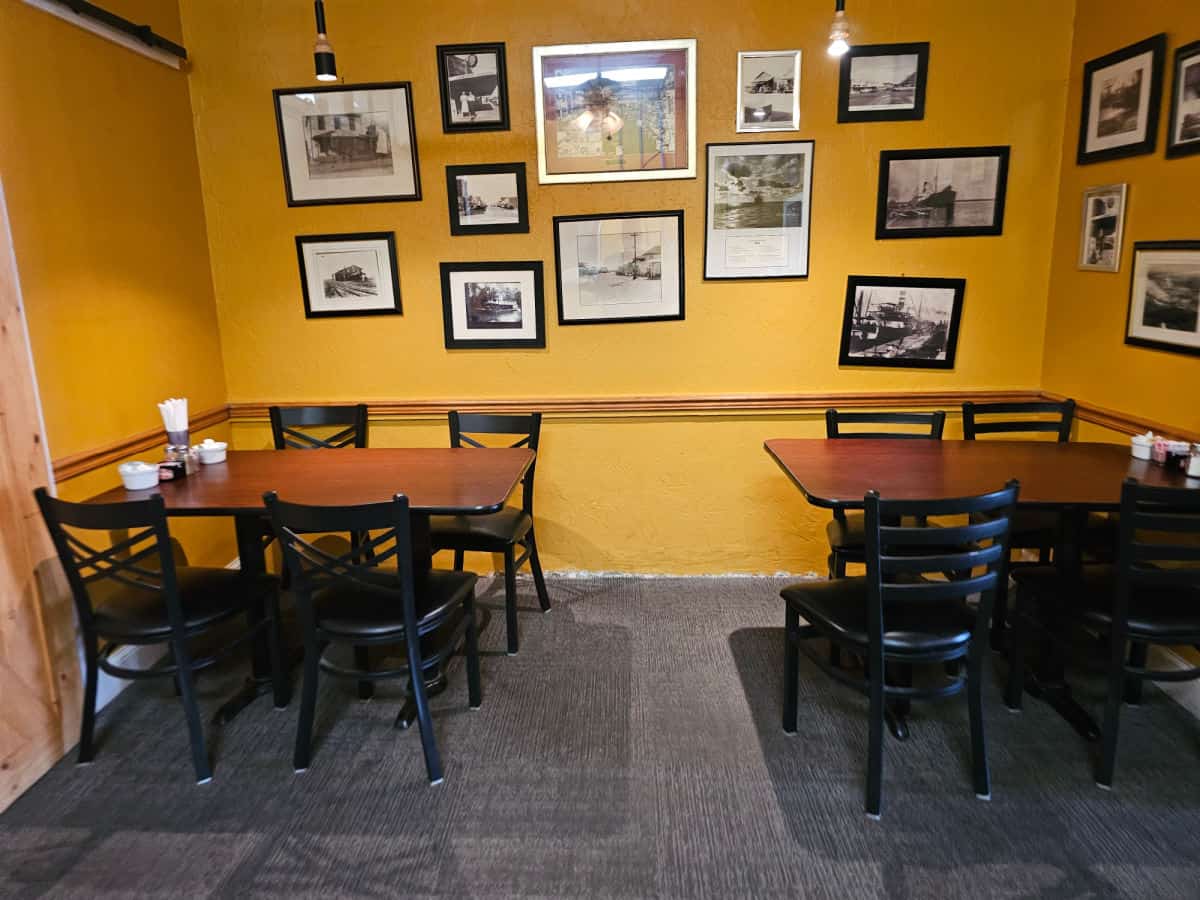 tables and chairs next to a yellow wall covered in framed photos