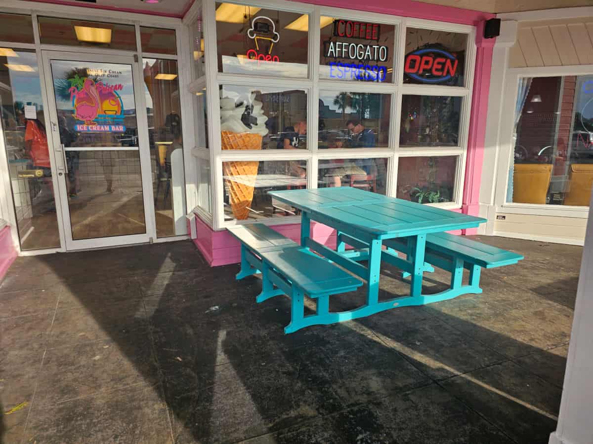 Blue picnic table outside of Pink Pelican Ice Cream bar with pink buiding