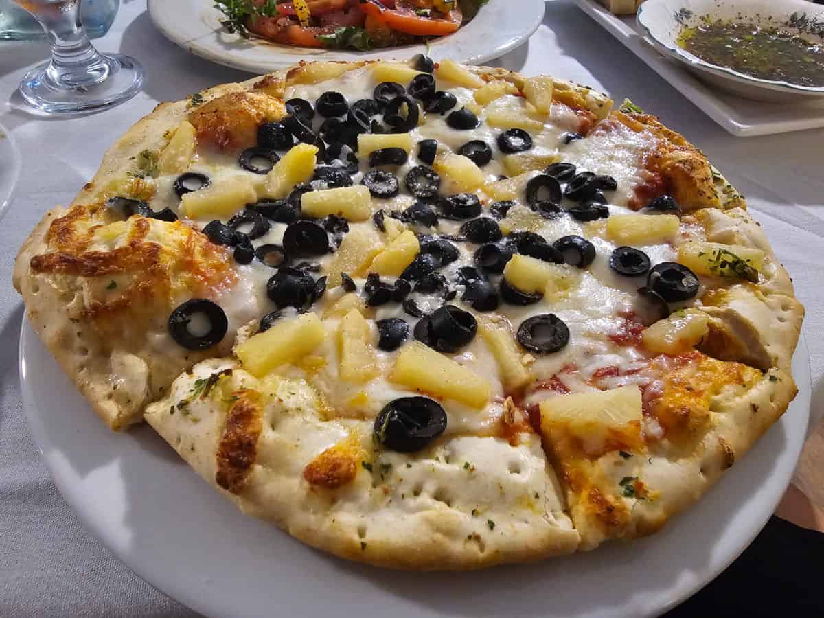 thin crust pizza with pineapple and black olive on a white linen table
