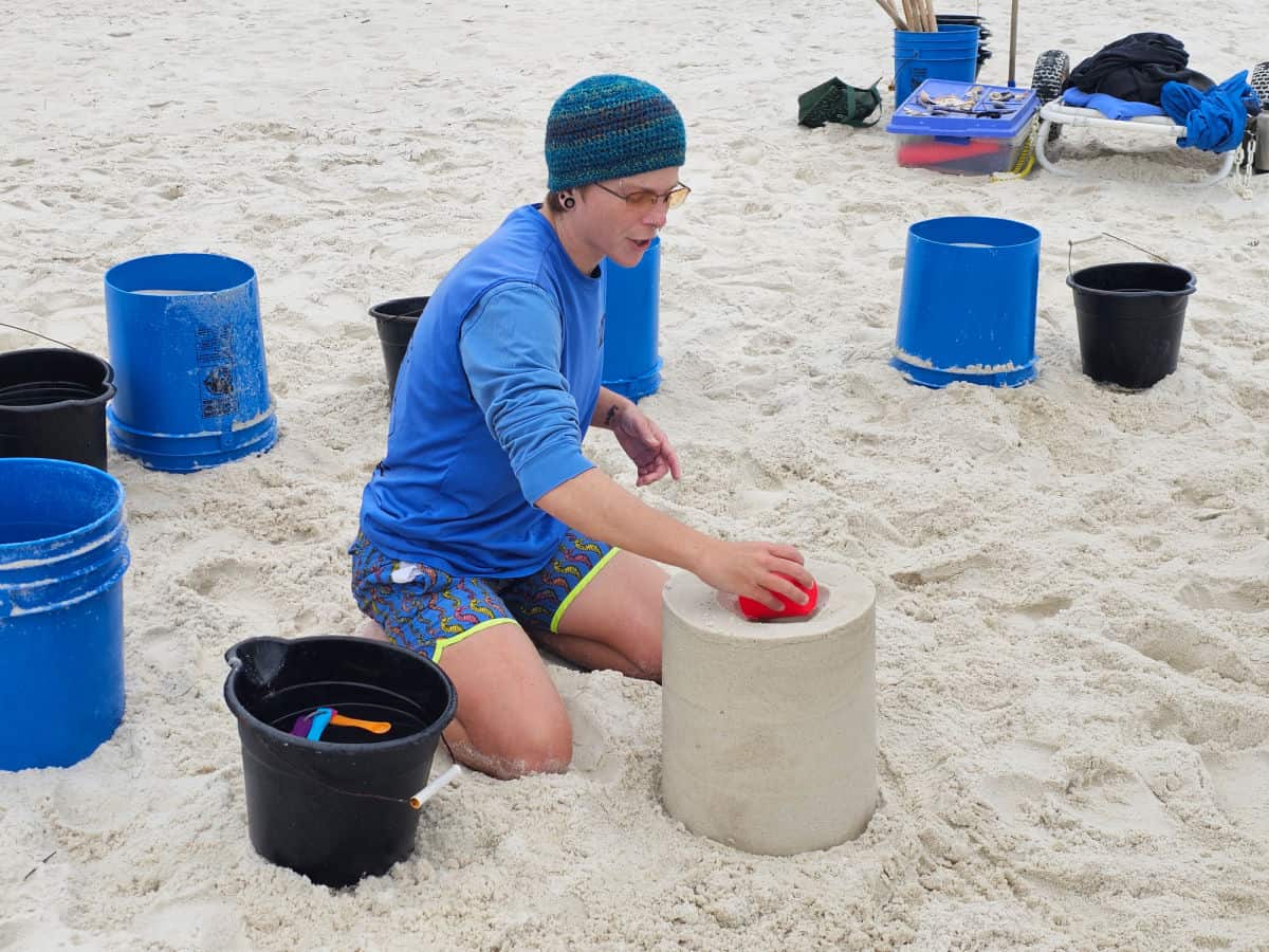 Sand Castle university instructor next to a sand castle with blue buckets