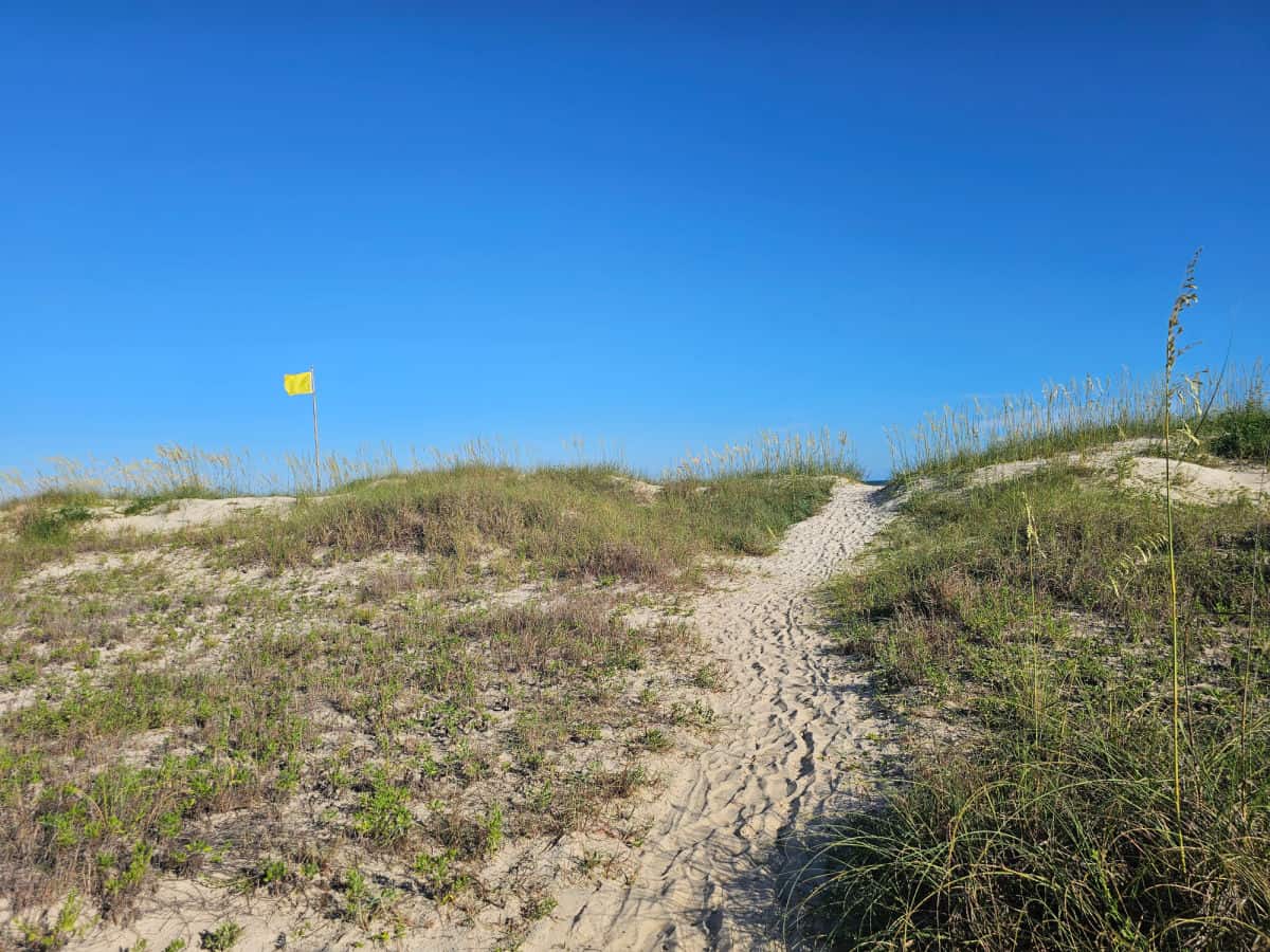 sand trail to the beach with a yellow warning flag
