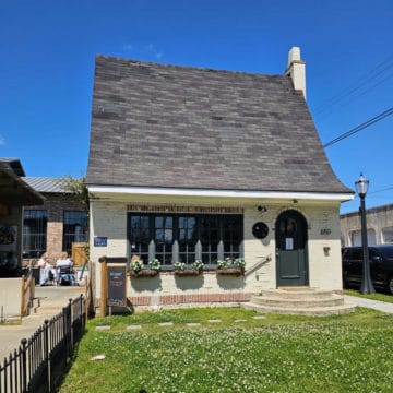 The cheese cottage exterior with steps to the front door and flowers in baskets by the window