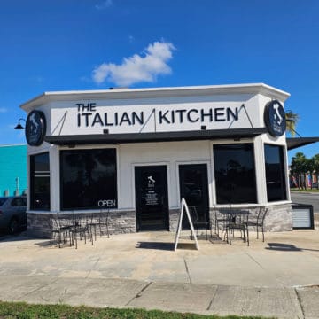 The Italian Kitchen sign over the entrance to the restaurant with tables and chairs ouside