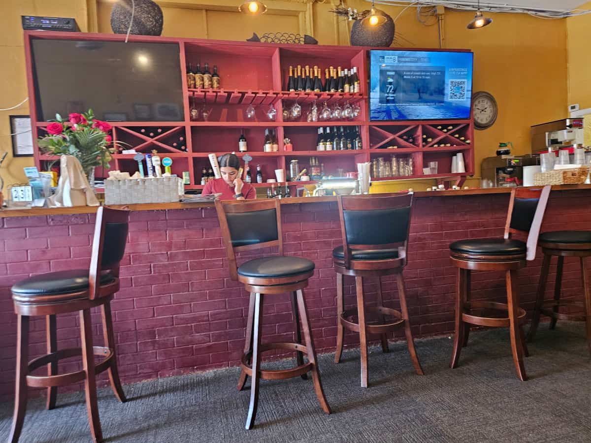 tall chairs next to a bar with a waitress on the phone behind the bar