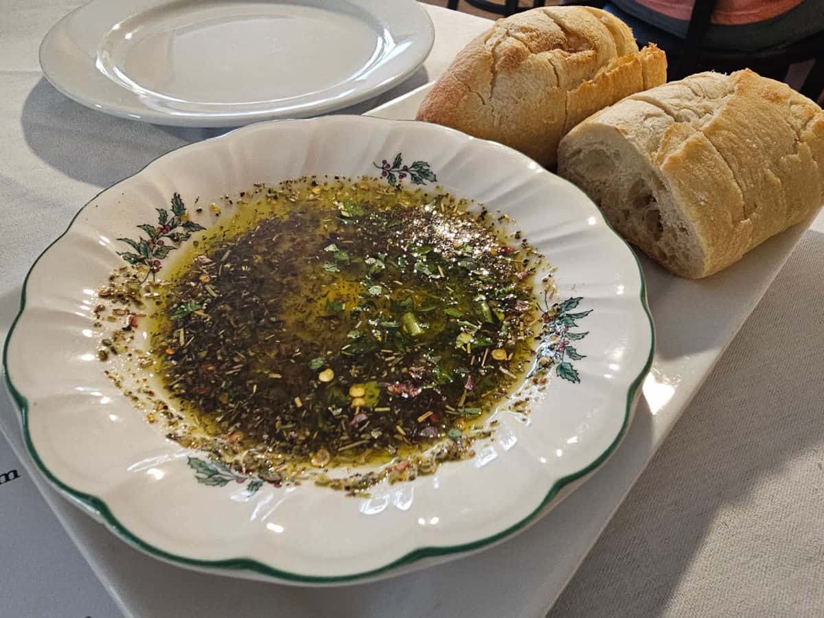 bread next to a bowl of dipping oil and herbs on a white platter