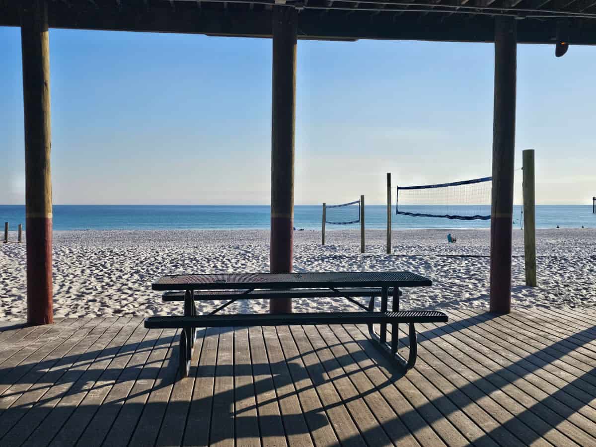 Picnic table under a cover with beach volleyball nets in the sand leading to the Gulf of Mexico