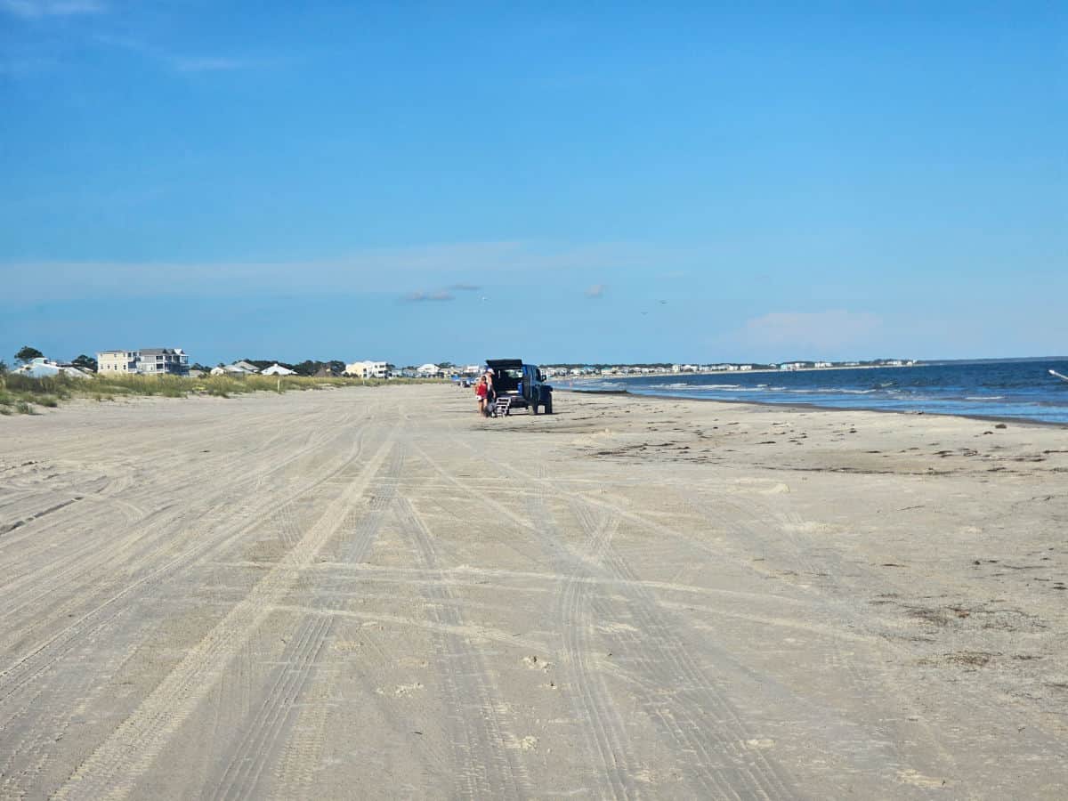 car driving on the sand with houses in the distance
