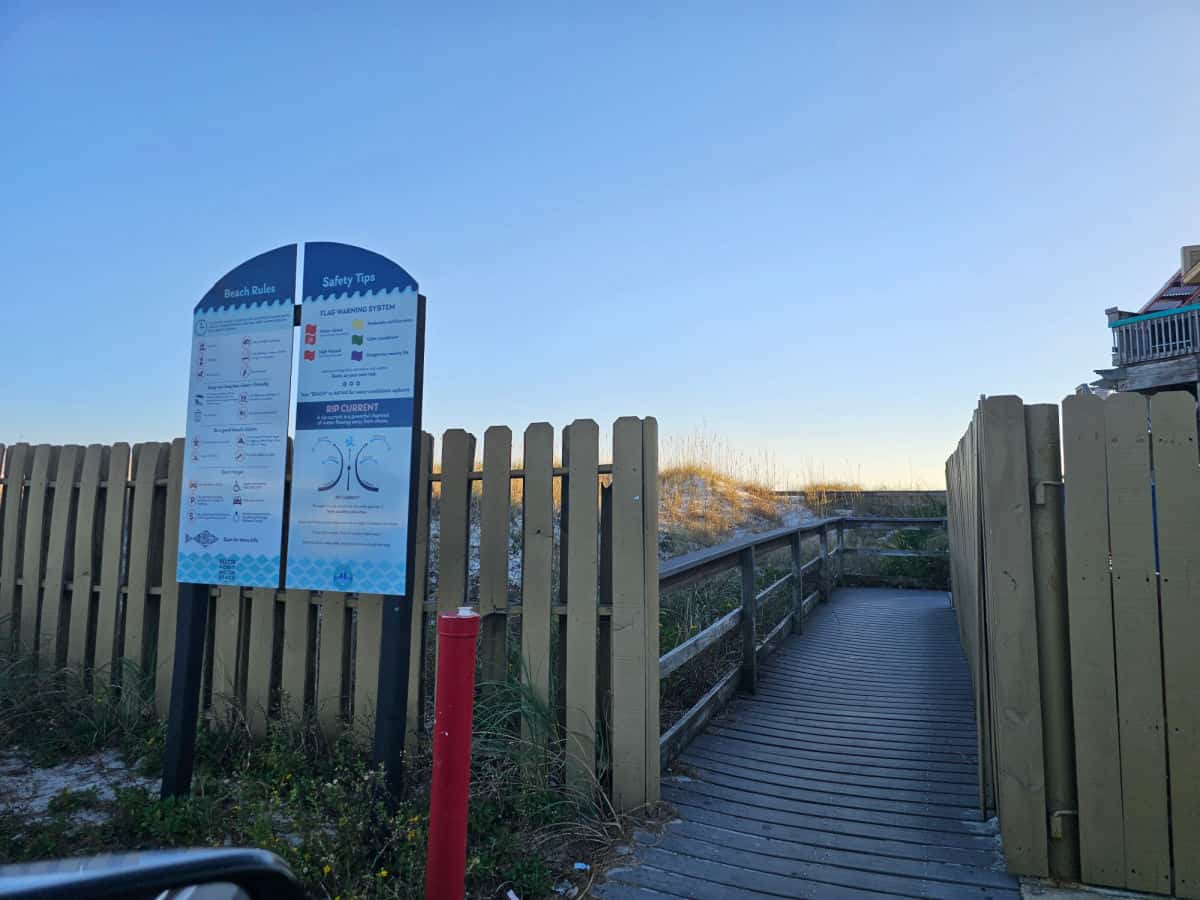 boardwalk leading to the beach with beach flag sign next to it
