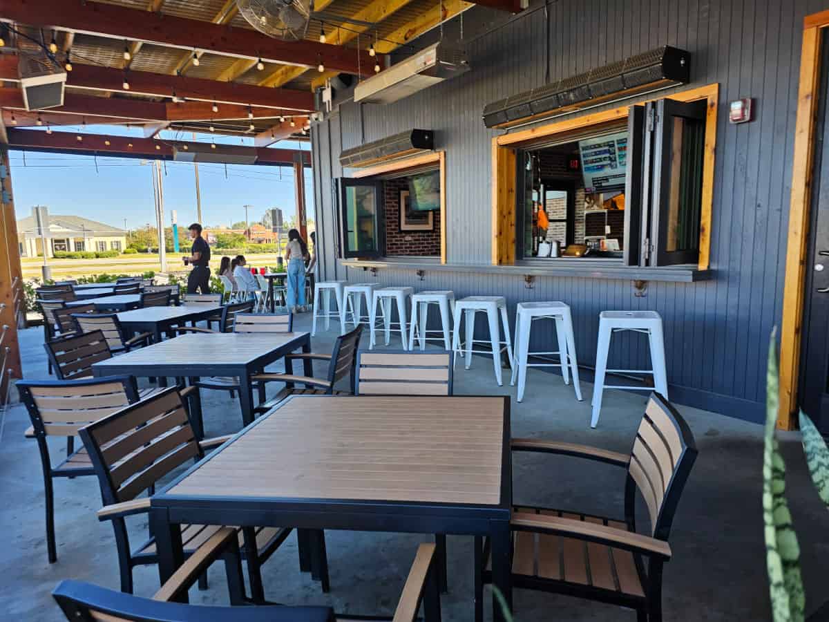 Outdoor seating with stools next to open windows along with tables and chairs