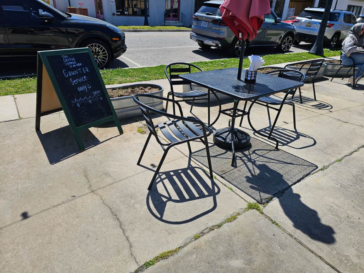 the cheese cottage outdoor seating with black tables and chairs near cars parked along the side of the road