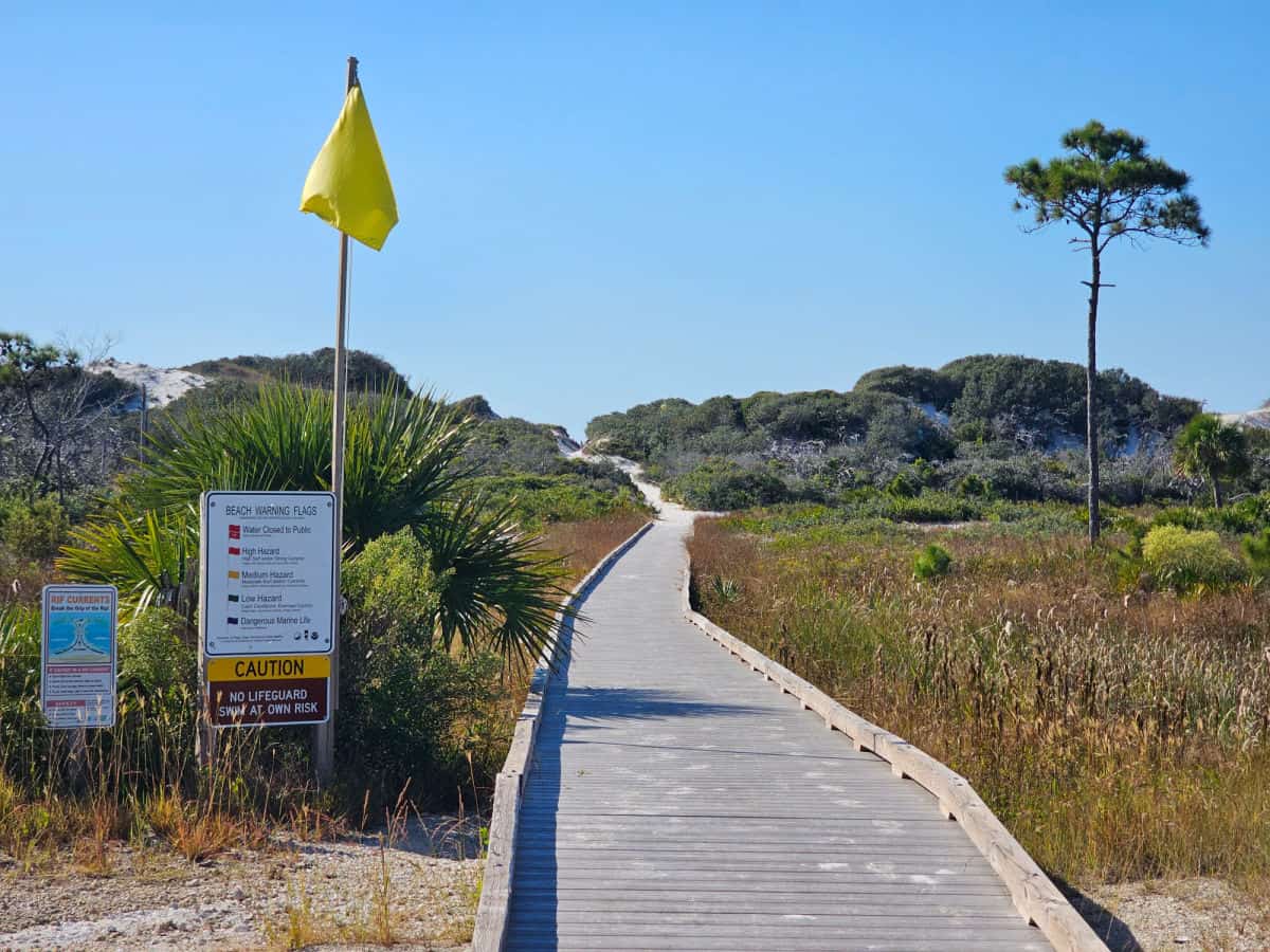 Yellow beach flag and warning sign next to a boardwalk leading to sand dunes