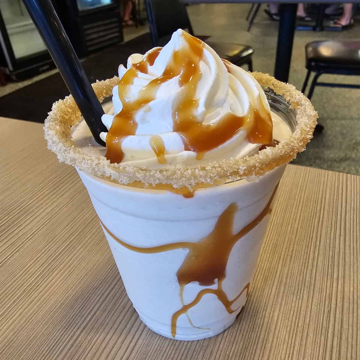 Salted Caramel Bushwacker with a salted caramel rim and dark straw on the table at Doc's Seafood Shack & Oyster Bar, Orange Beach