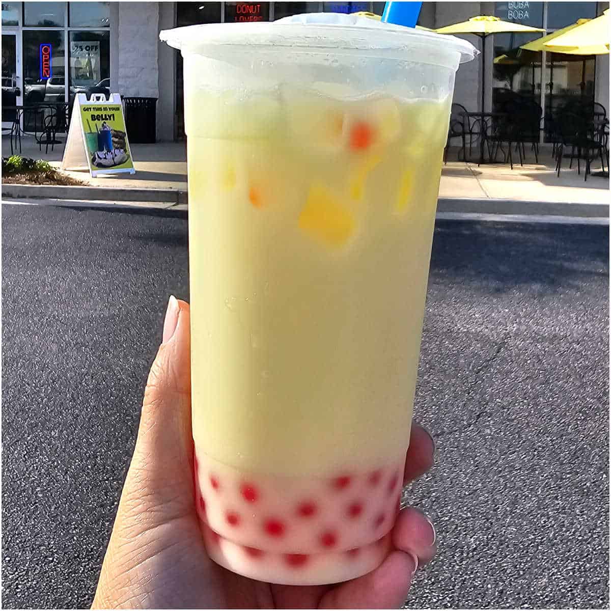 Yellow fruit tea with red popping boba being held in front of a restaurant.