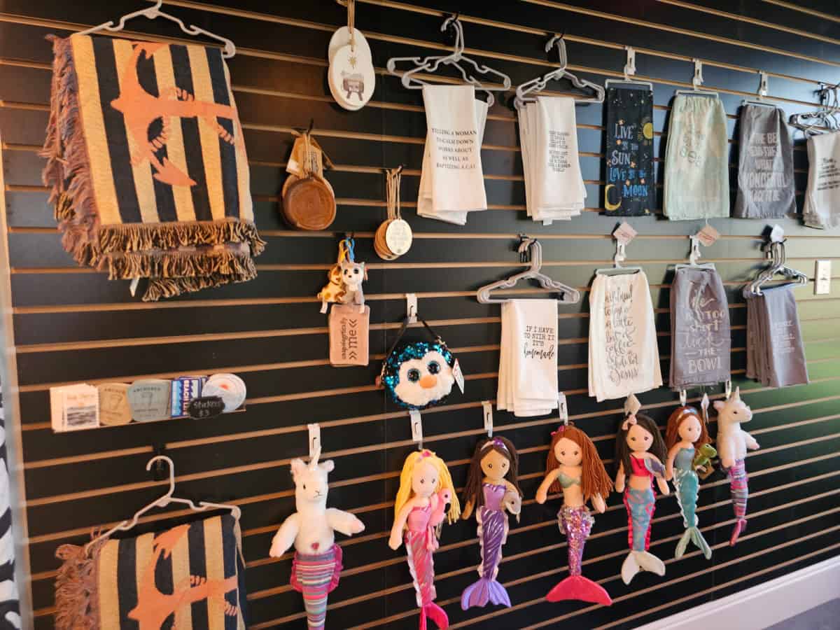 Wall with towels, mermaid dolls, stickers, and blankets in Anchored Coffee House