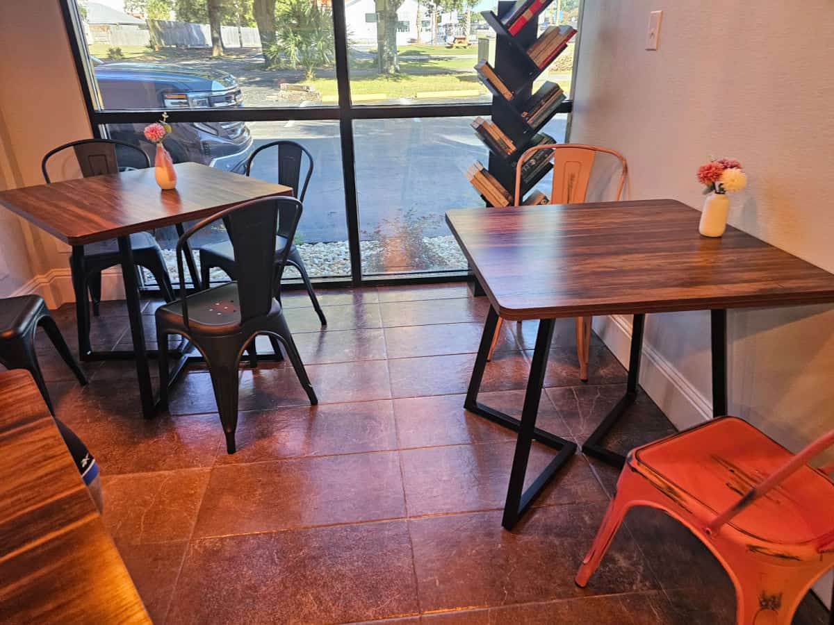 Indoor seating with tables and metal chairs, a shelf of books in the background in Anchored Coffee house