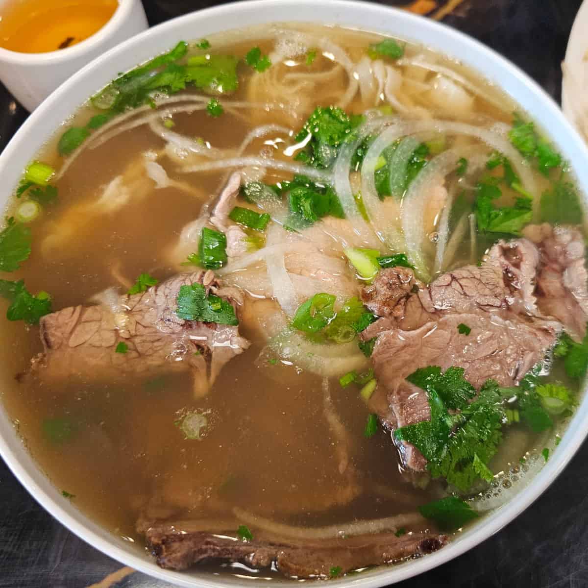 Steak pho in a white bowl filled with noodles and broth