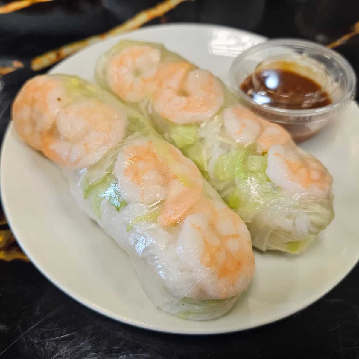 Two Shrimp Spring Rolls on a white plate with a container of sauce at Pho Mo