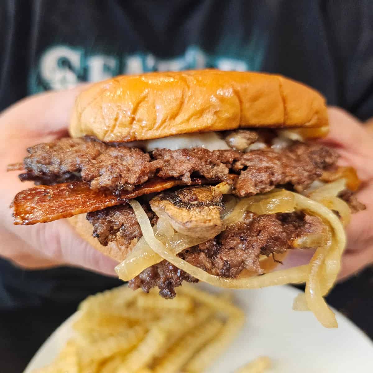 Small Town Big Beach Burger with bacon, two smashburgers, onions, and cheese held over a plate of french fries