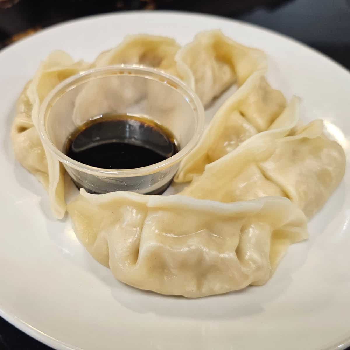 Steam Pork Dumplings on a white plate with a container of sauce from Pho Mo