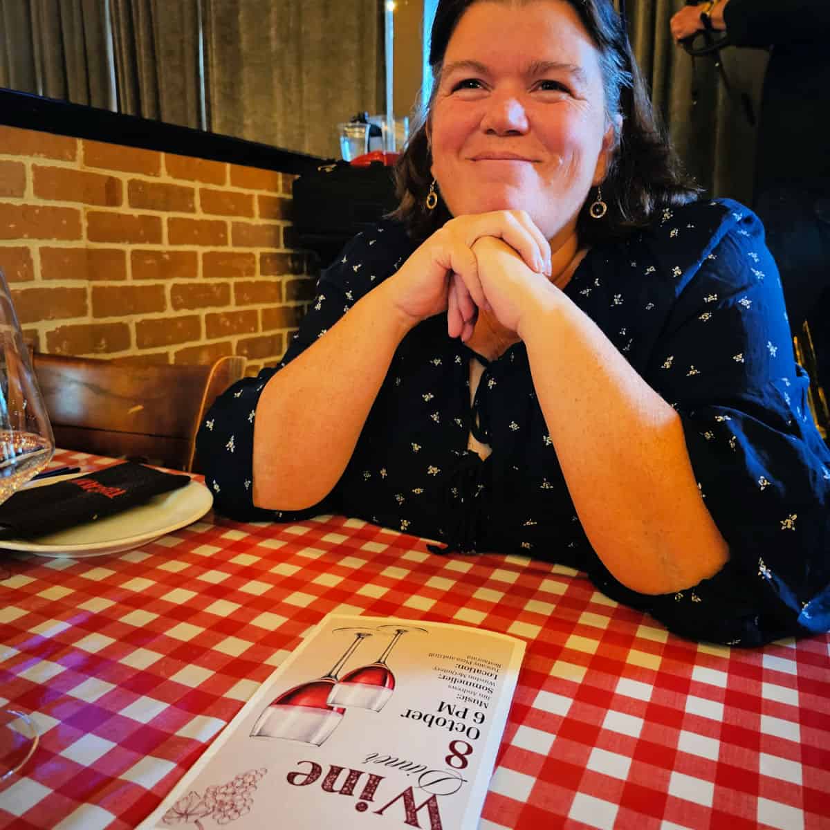 Tammilee in a blue shirt at the Tuscany Wine Dinner with a menu in front of her