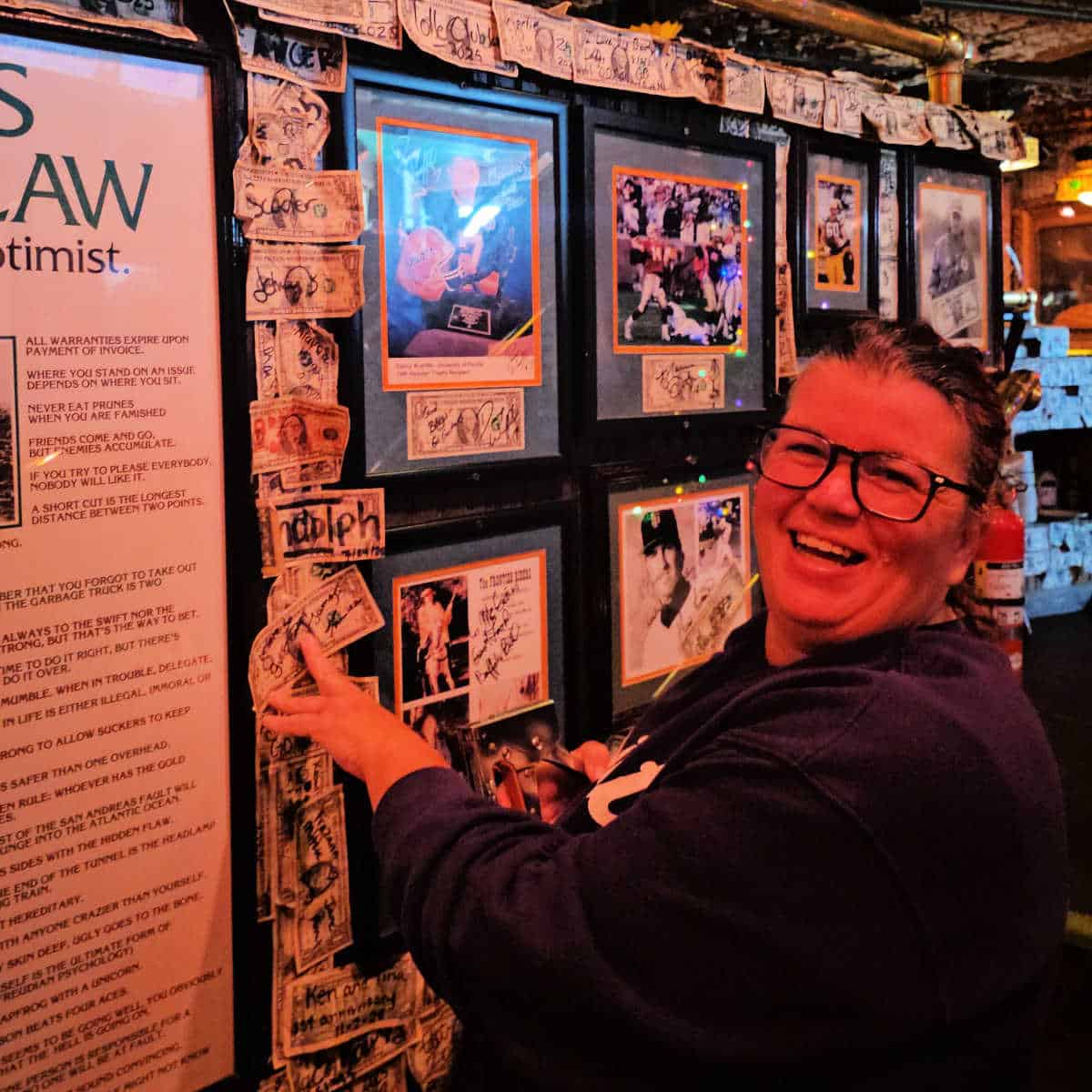 Tammilee stapling a dollar bill to the wall in McGuire's Irish Pub in Destin with dollar bills and photos on the wall around her