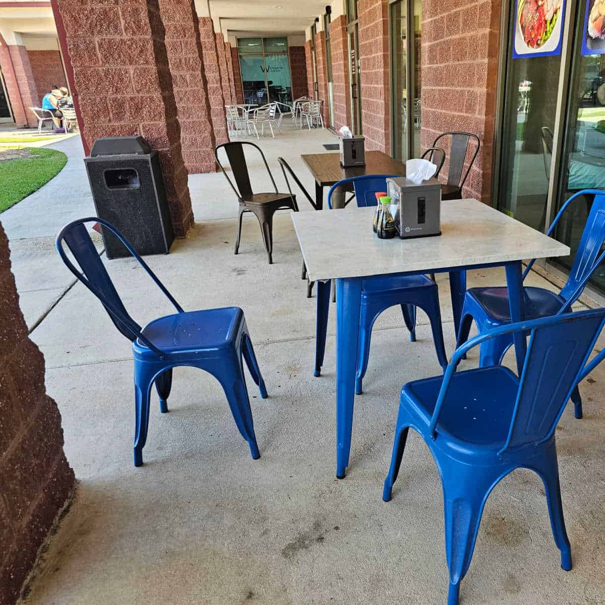 poke bowl sushi burrito & boba outdoor seating with tables, blue and black chairs along the side of a brick building