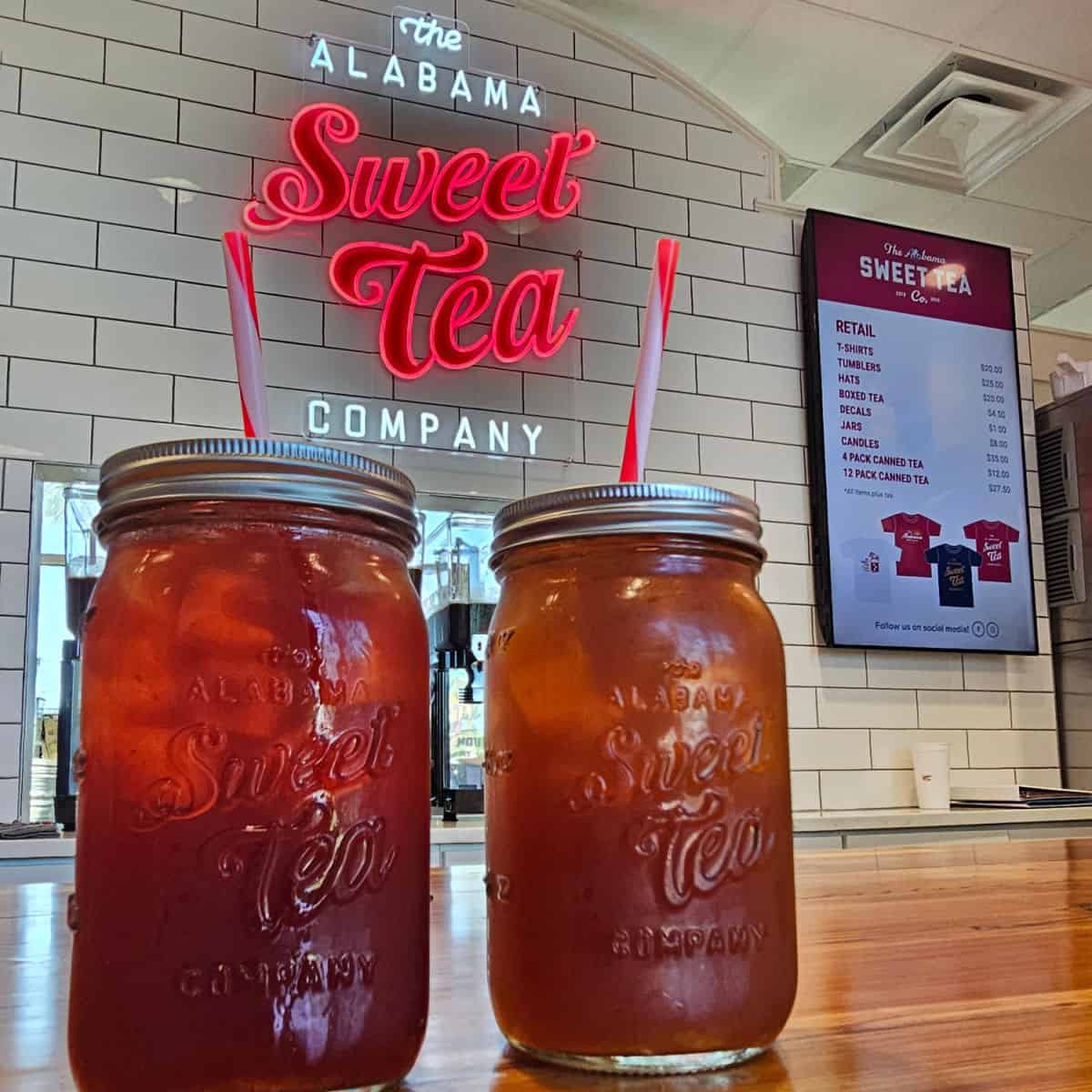 The Alabama Sweet Tea Company neon sign on a white tile wall with two mason jars with tea on a counter
