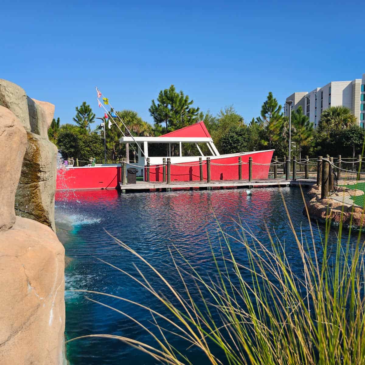 Looking over the water to a red boat that is a mini golf hole