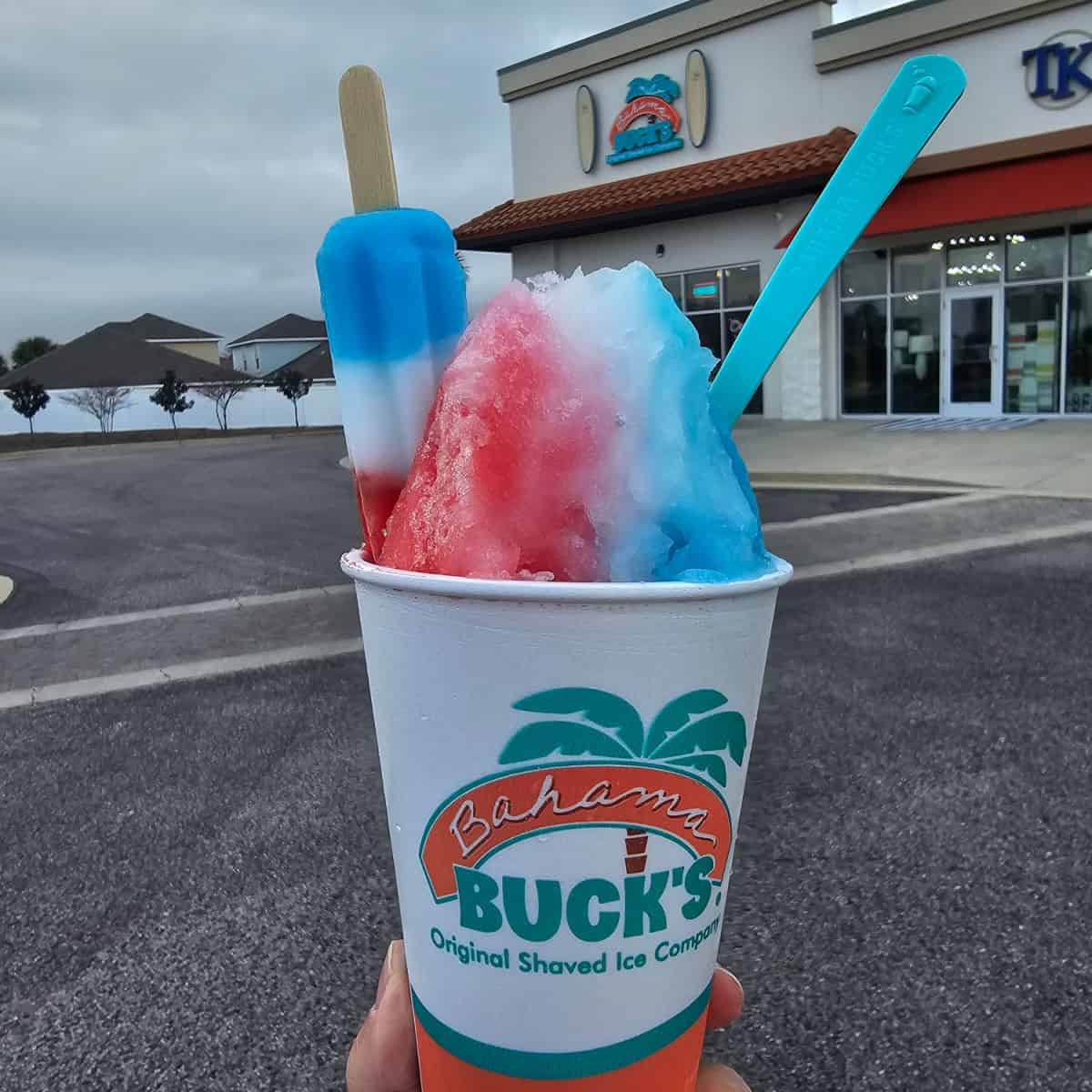 Bomp Pop sno with a Bomb Pop posicle and blue spoon in front of Bahama Bucks Orange Beach