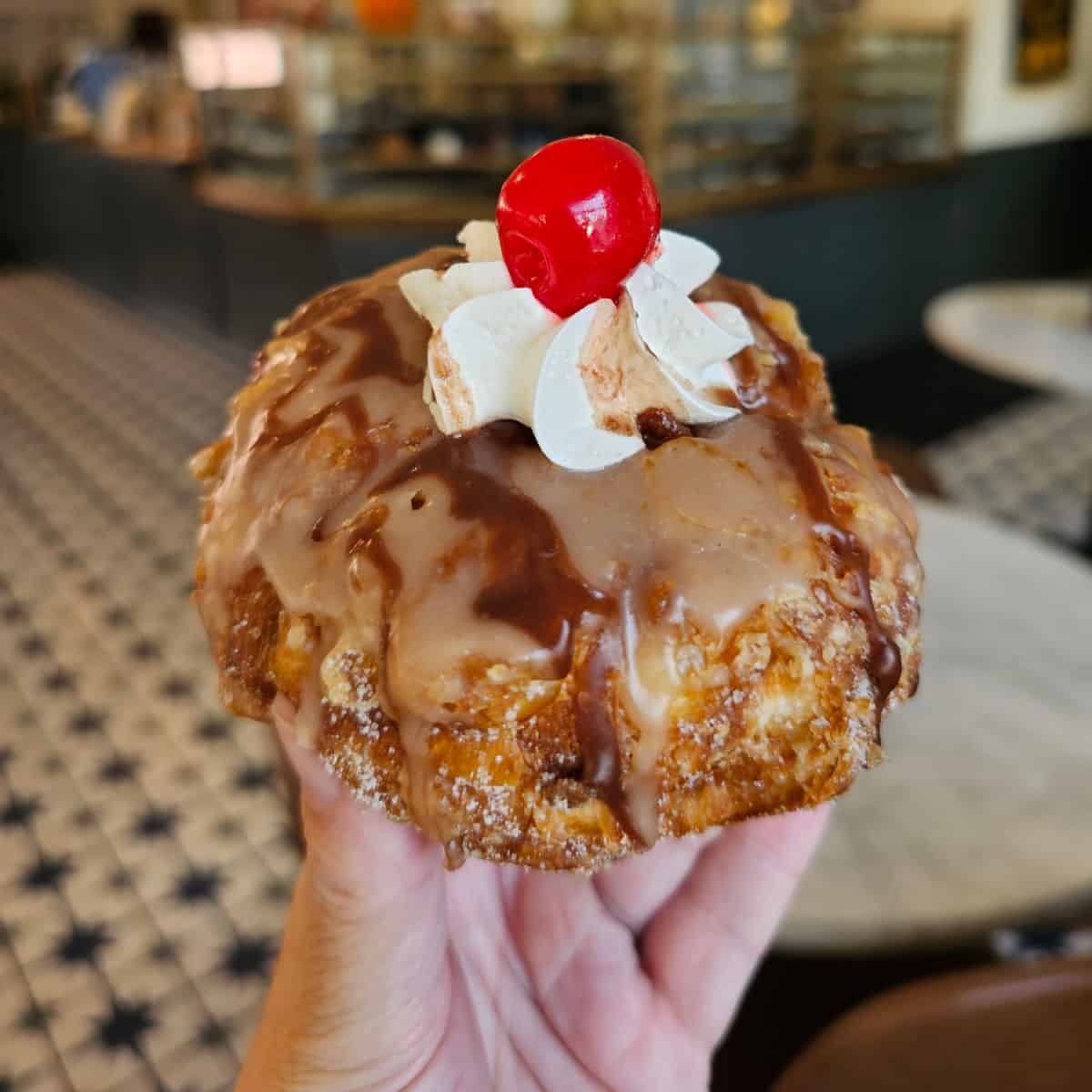 hand holding a bushwacker donut topped with whipped cream and a cherry in Parlor Donuts Gulf Shores