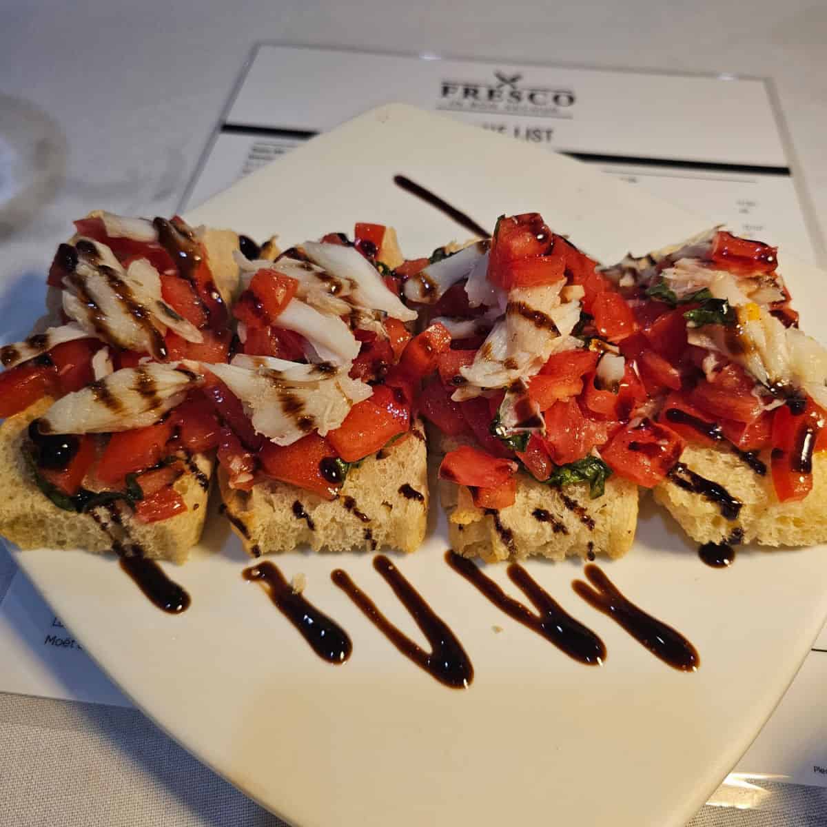 crab bruschetta on a white plate drizzled with balsamic vinegar sitting on a Fresco menu