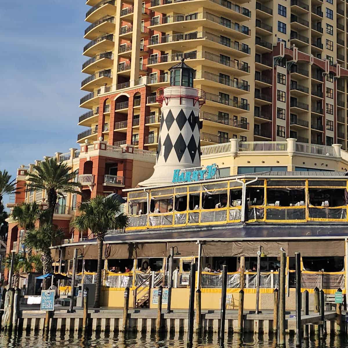 Harry T's blue restaurant sign just under the black and white lighthouse on top of the restaurant, open air seating on two levels below the sign as seen from the water