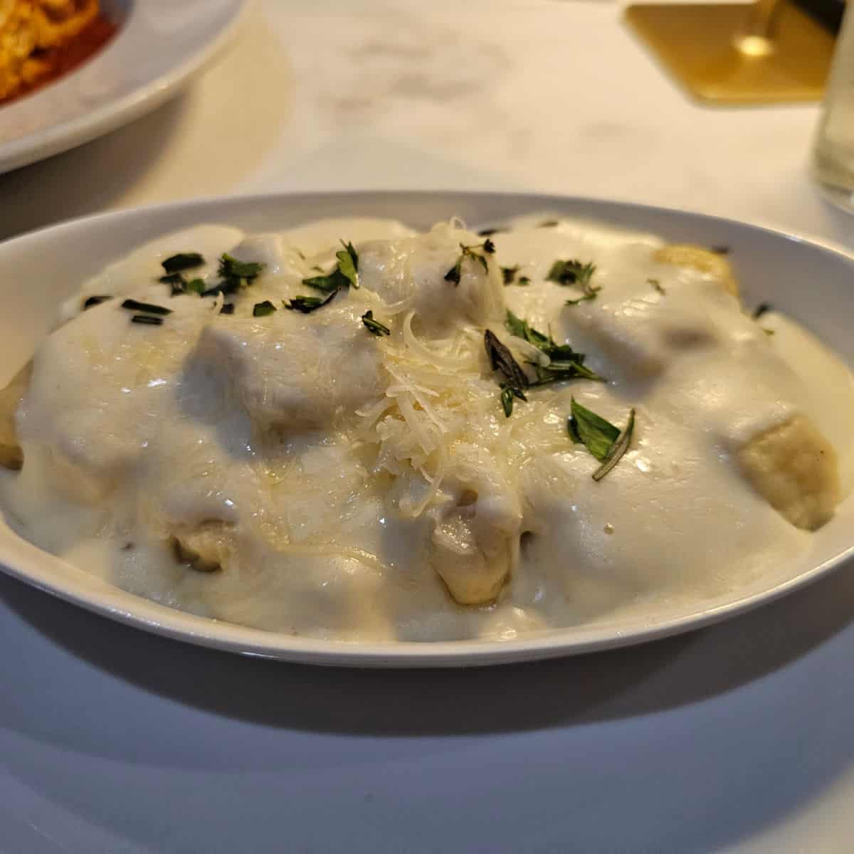 Potato gnocchi topped with creamy white sauce and cheese in a white bowl