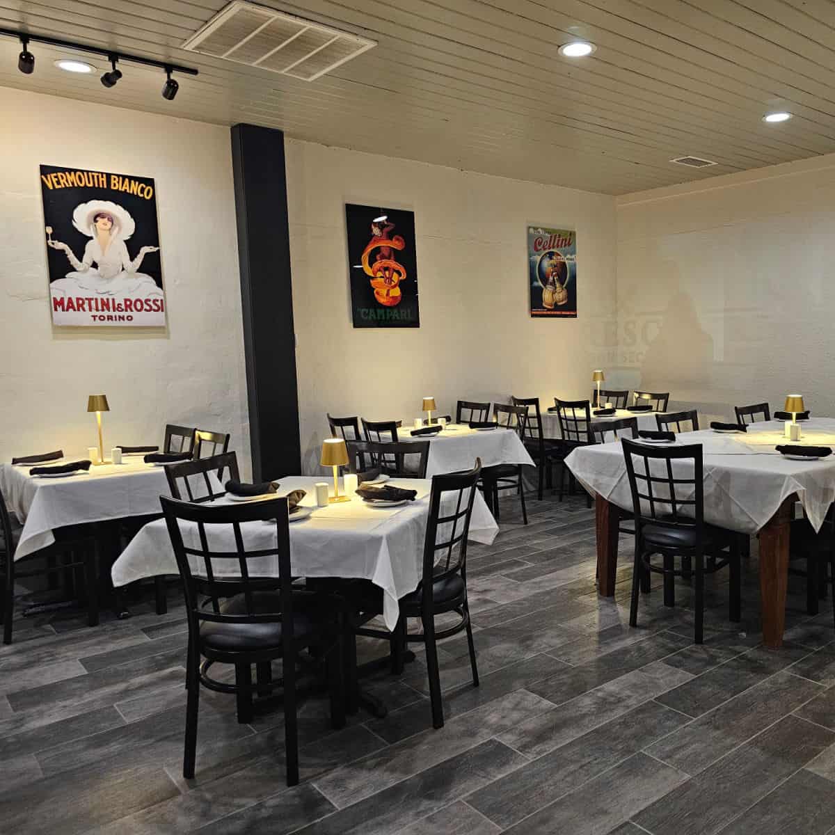 Indoor tables with white tablecloths and black chairs, Italian posters on the wall