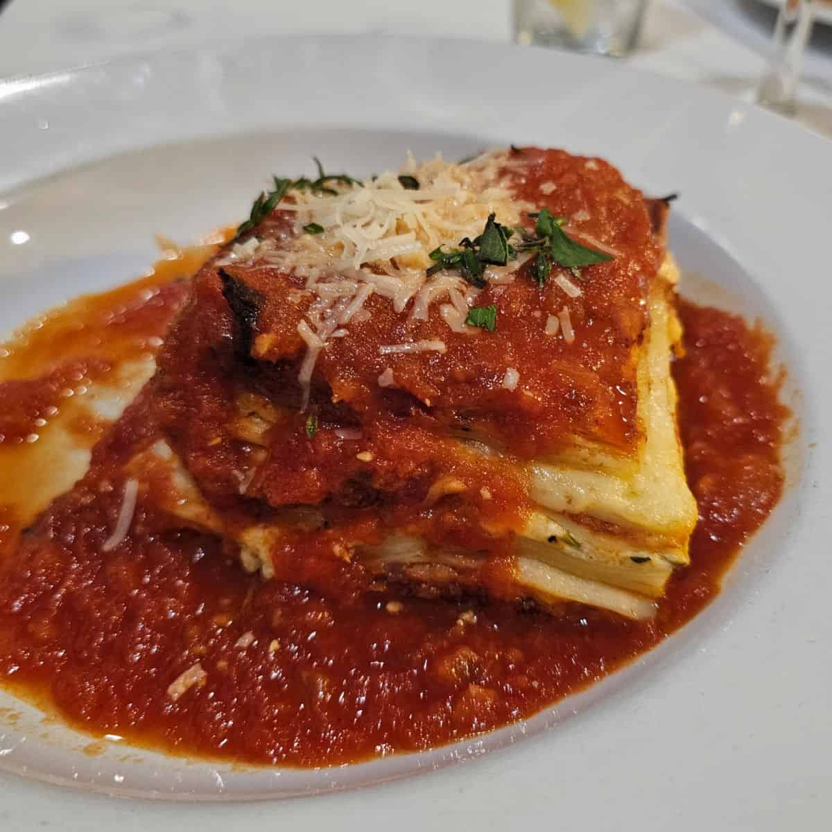 Lasagna with red sauce and cheese garnish in a white bowl