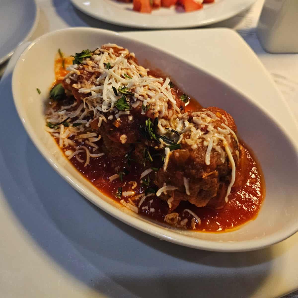 Beef meatballs with cheese and tomato sauce in a white bowl on a white plate at Fresco