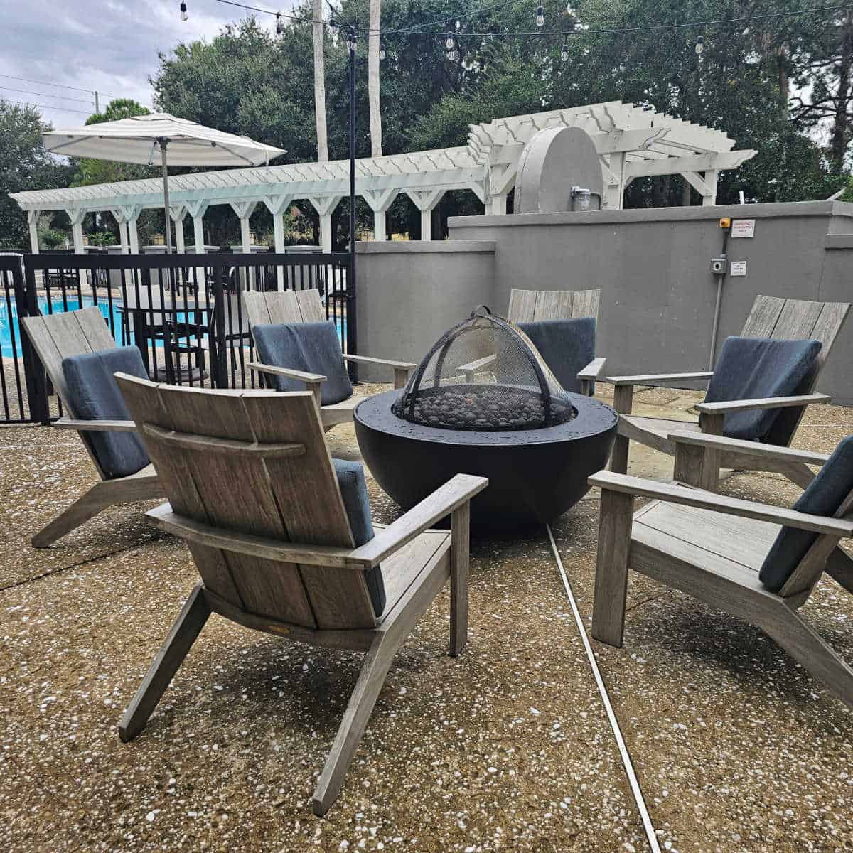 outdoor fireplace with Adirondack chairs around it next to the outdoor pool