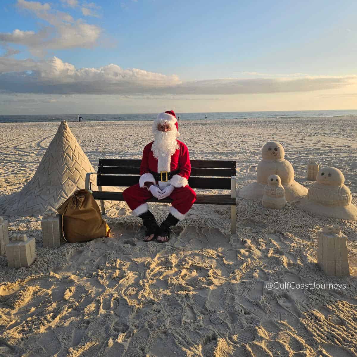 Santa sitting on a bench with a sand Christmas tree, snowmen and gifts