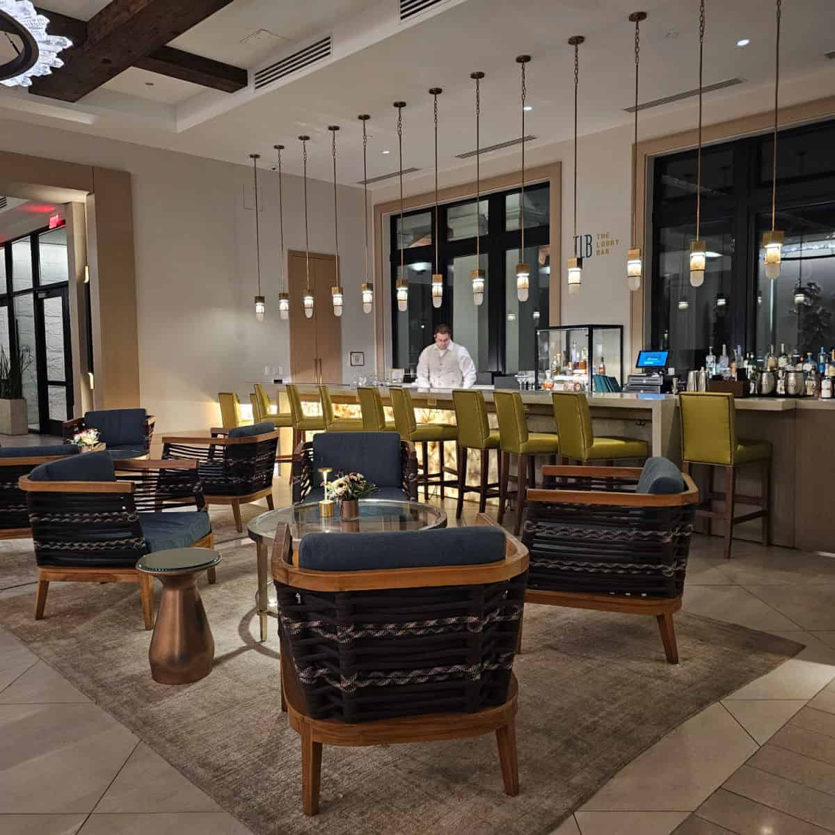 the lobby bar with a bartender behind the counter, tall bar stools with backs against the bar, blue chairs with glass tables nearby