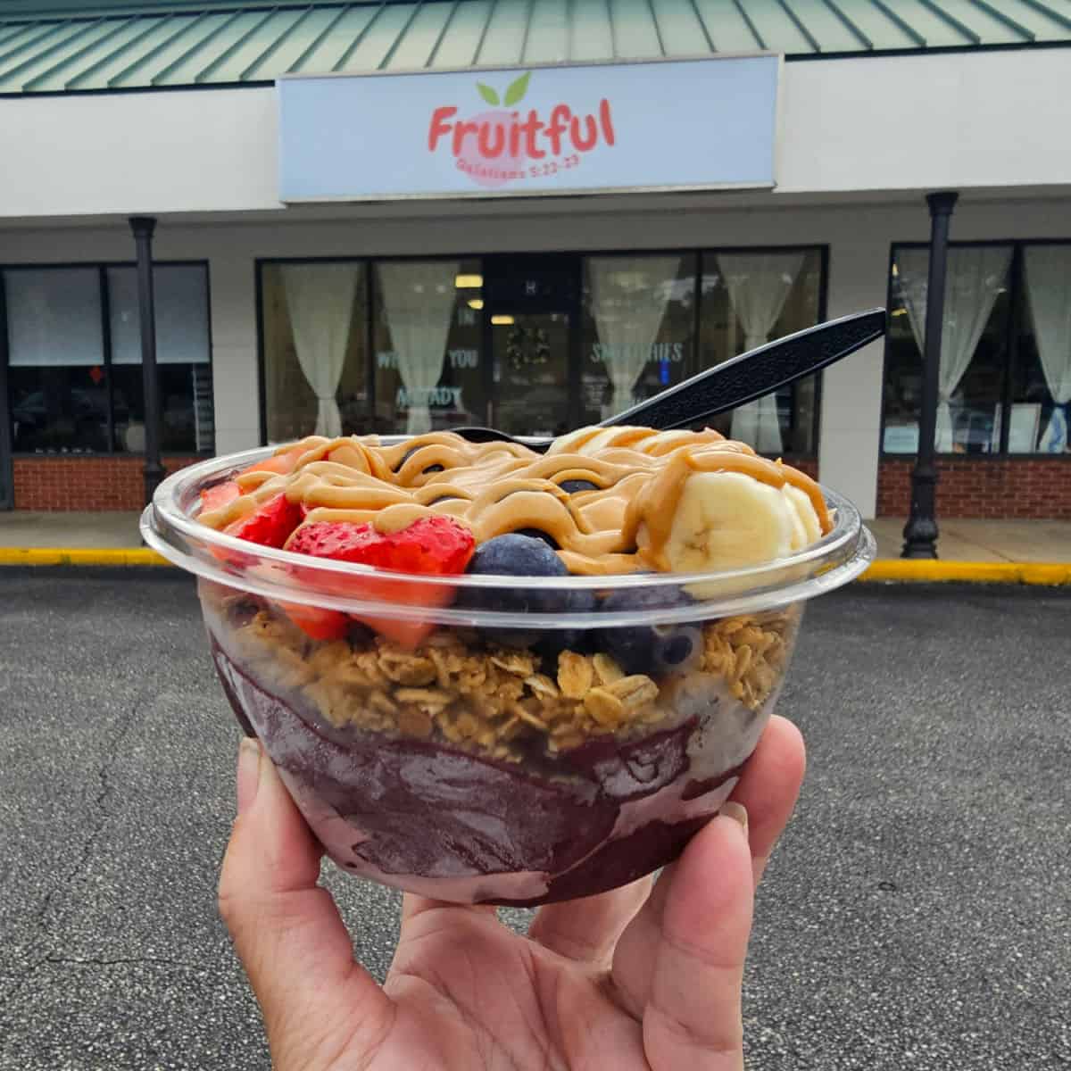 hand holding an acai bowl in front of the fruitful sign and store entrance