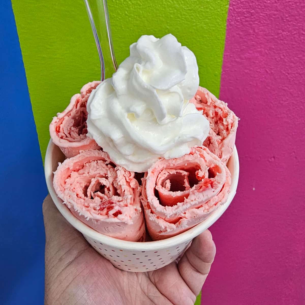 hand holding a cup with cherry rolled ice cream topped with whipped cream