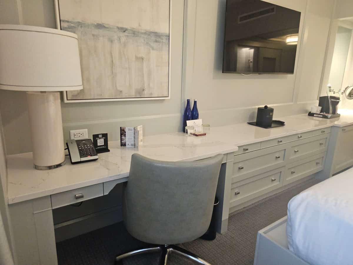 Desk are with chair and lamp connected to a dresser, flatscreen tv on the wall, keurig on the couter top